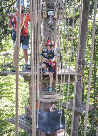 Children enjoying climbing at Söllereck adventure park, surrounded by trees, with safety gear, supervised by an adult. | © Oberstdorf · Kleinwalsertal Bergbahnen