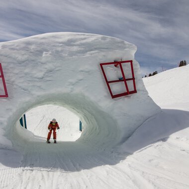 Große Schneeskulptur in Form eines Kopfes mit roten Fenstern, im Skigebiet Oberstdorf/Kleinwalsertal, mit einem Skifahrer darunter. | © Kleinwalsertal Tourismus eGen • Oberstdorf Kleinwalsertal Bergbahnen