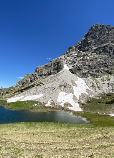 Mountain scenery with a small lake in the foreground and a large mountain peak in the background under a clear blue sky. | © Kleinwalsertal Tourismus eGen