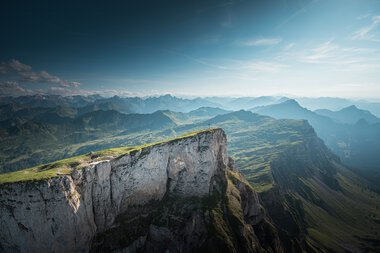 Berglandschaft mit grünen Hügeln und steilen Klippen unter einem blauen Himmel, aufgenommen vom Ifen. | © Kleinwalsertal Tourismus eGen • Fotograf: Robert Niederwolfsgruber