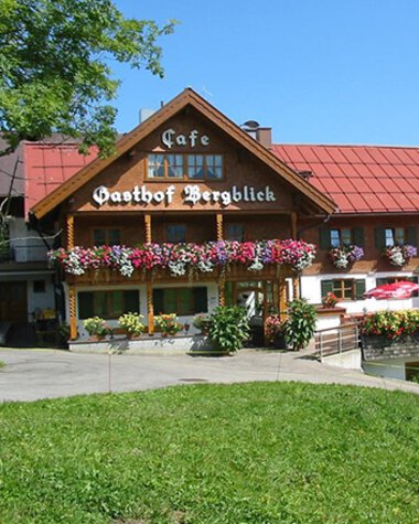 Bergblick Gasthof mit Blumen und Terrasse im Kleinwalsertal, mit einer Ziege im Vordergrund und Hügel im Hintergrund. | © Kleinwalsertal Tourismus eGen