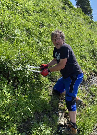 Young woman trimming branches in greenery on a steep roadside during a volunteer activity in July 2021. | © Kleinwalsertal Tourismus eGen